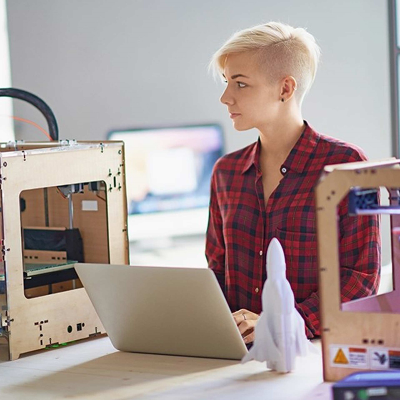 Junge Frau mit Laptop zwischen zwei 3D-Drucker