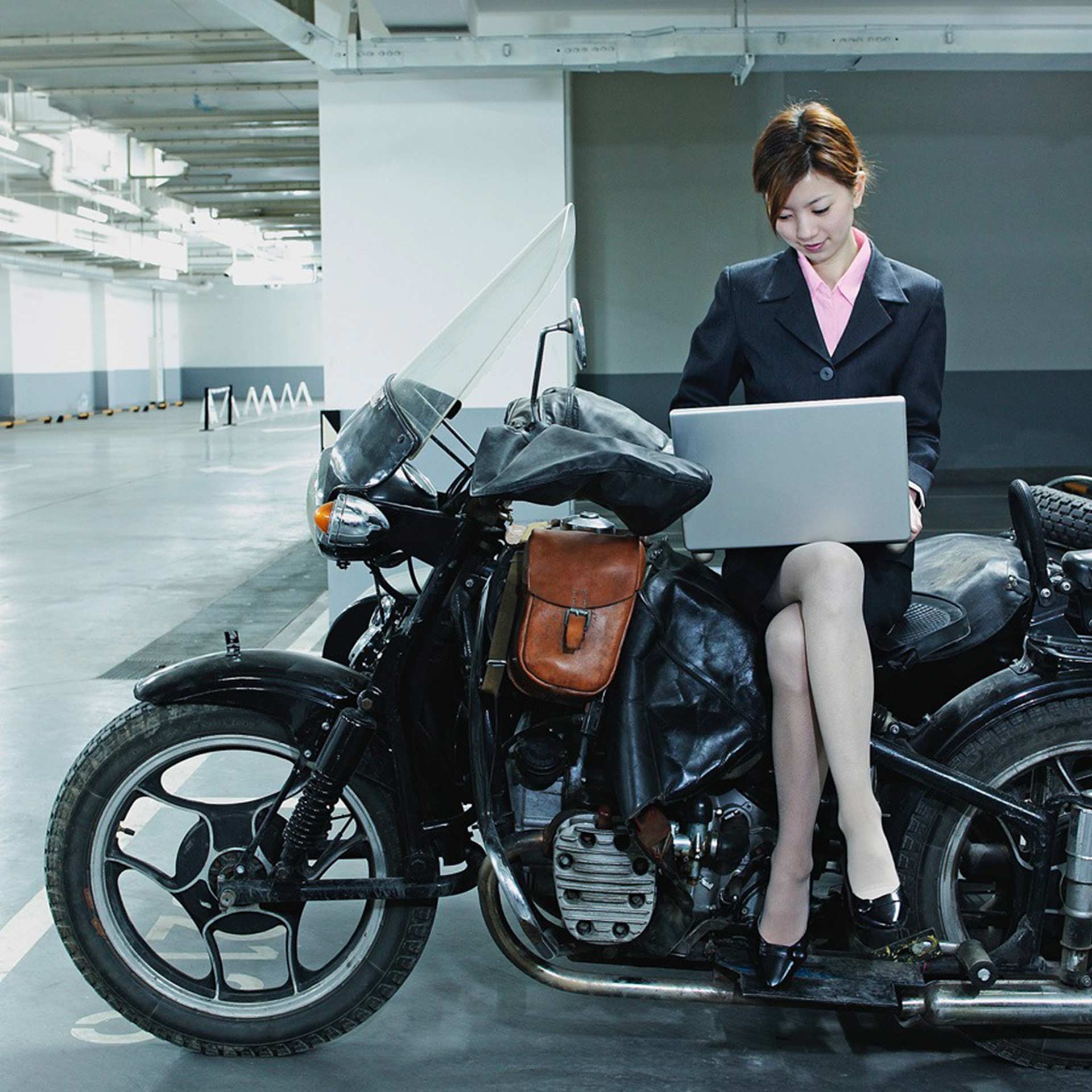 Businessfrau seitlich sitzend auf einem Motorrad mit Laptop auf ihrem Schoss