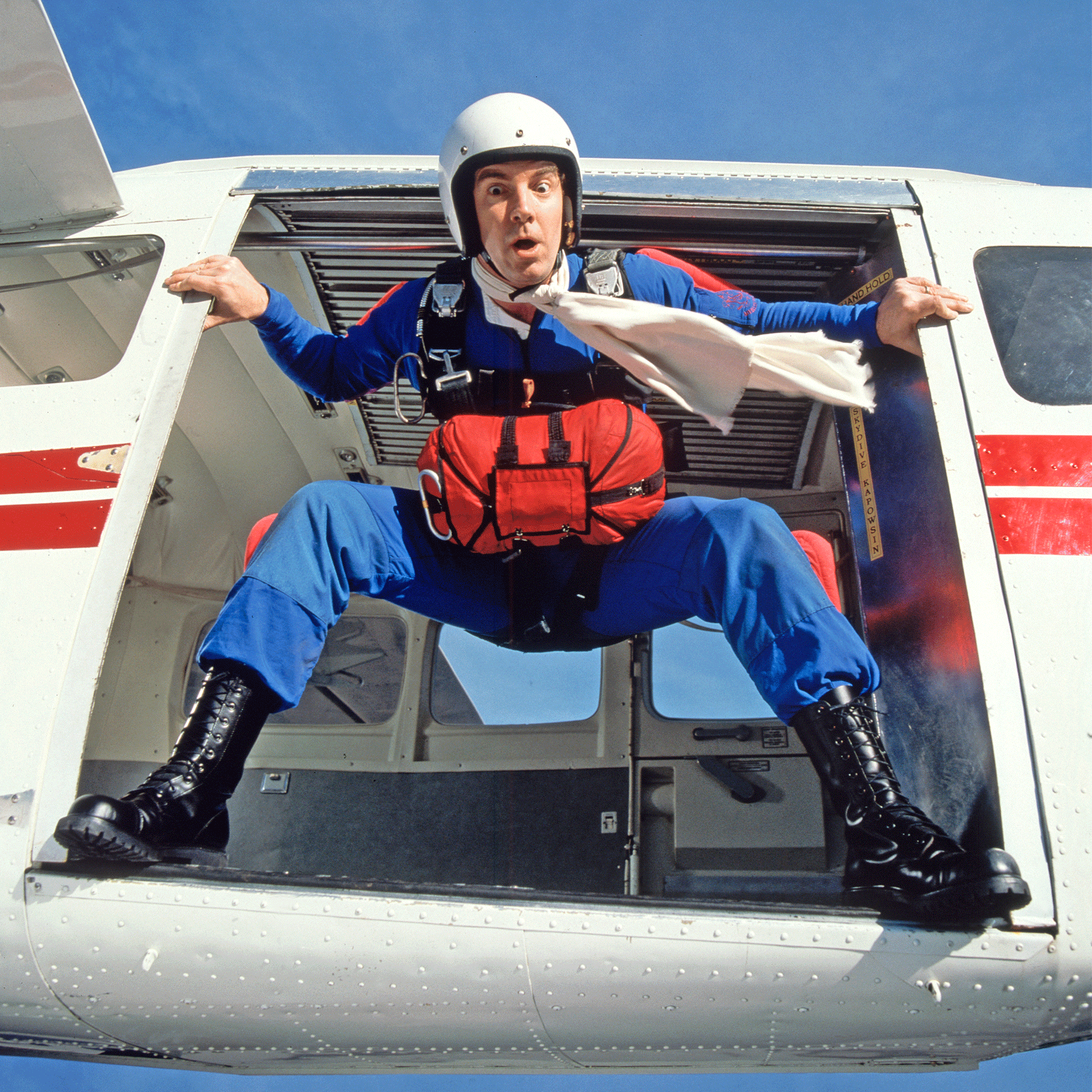 Ein Fallschirmspringer im blauen Overall steht in einem Kleinflugzeug in der Tür und steht kurz vor dem Sprung