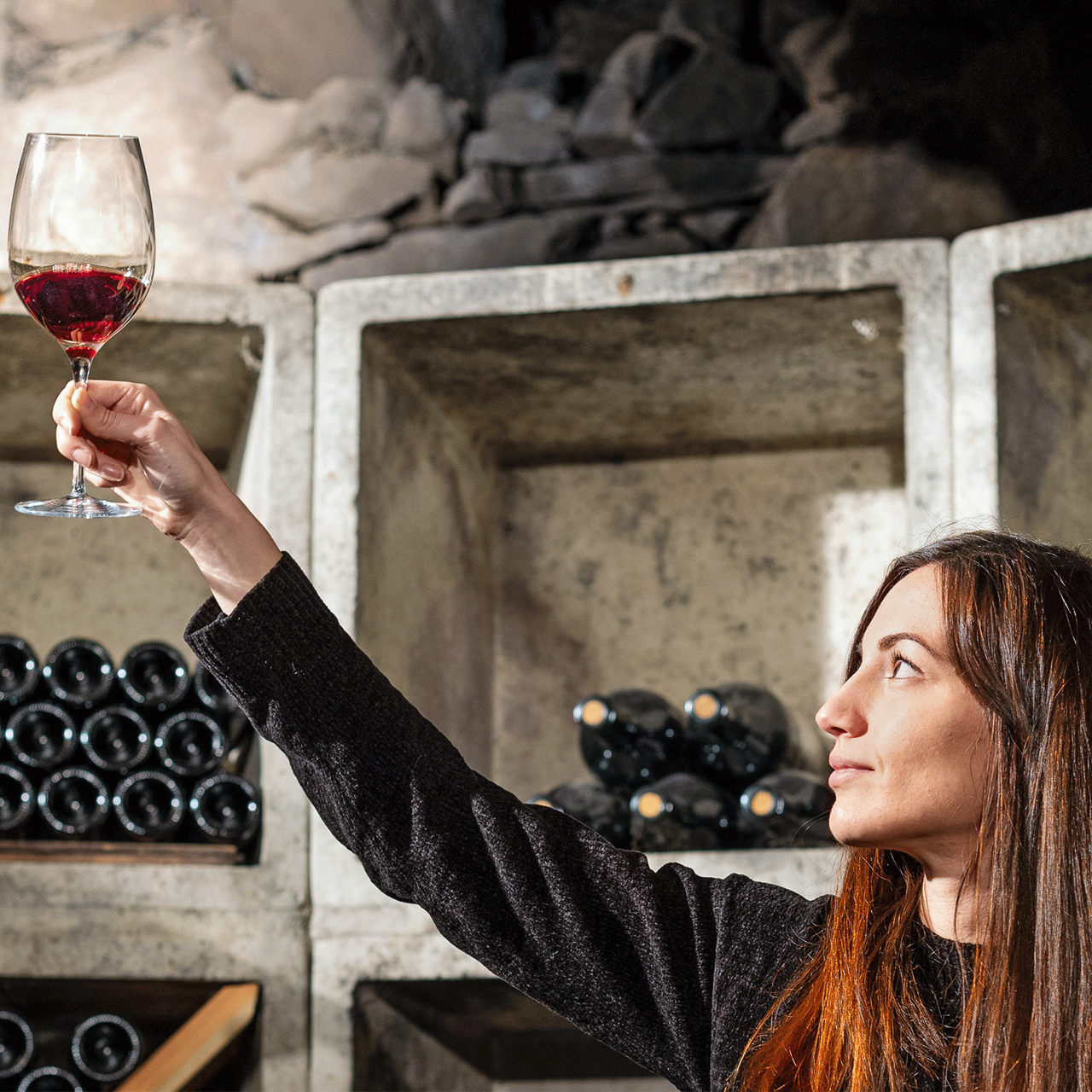 Frau im Weingut begutachtet ein Glas mit Wein im Licht