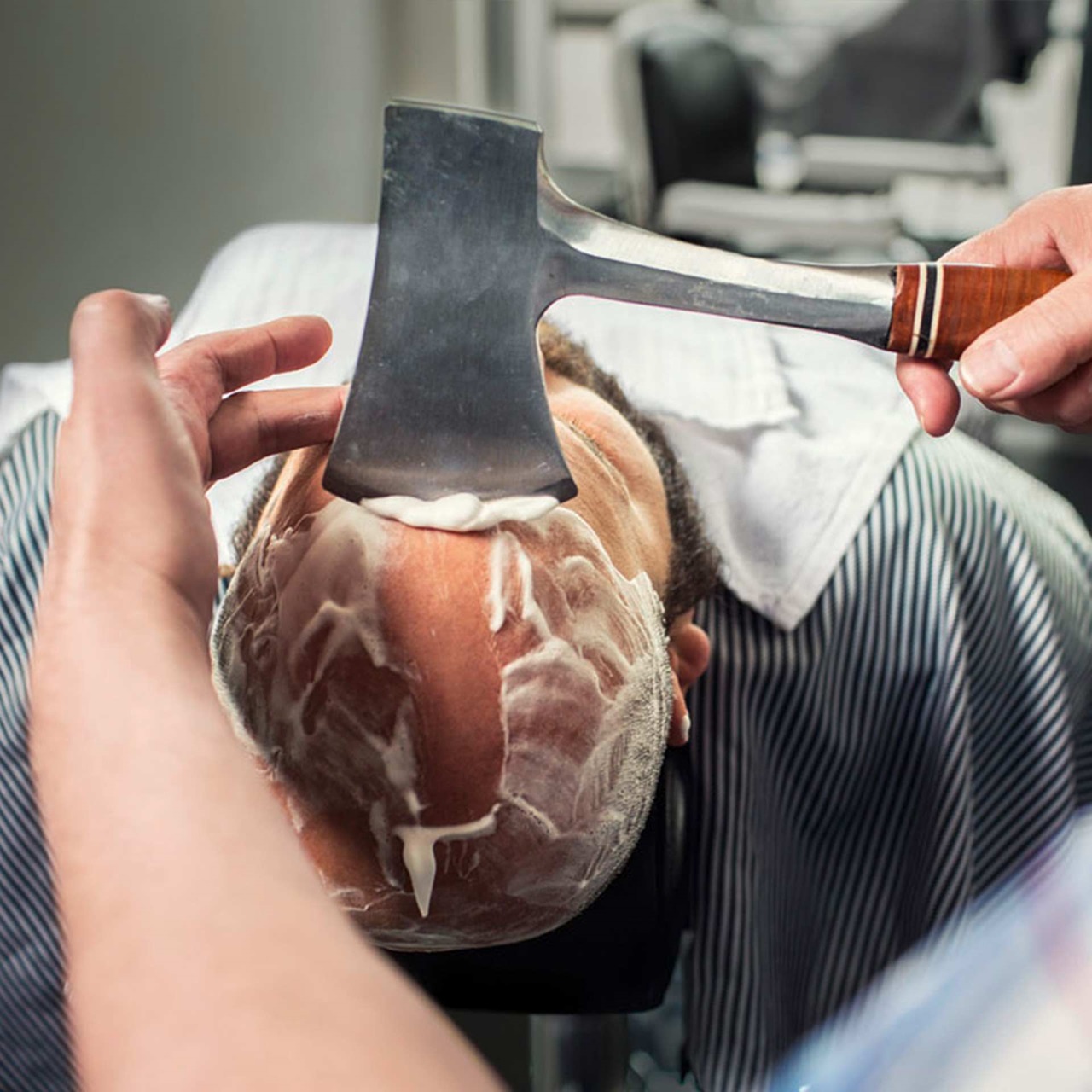 Barbier rasiert einem liegenden Mann die Haare mit einem Beil