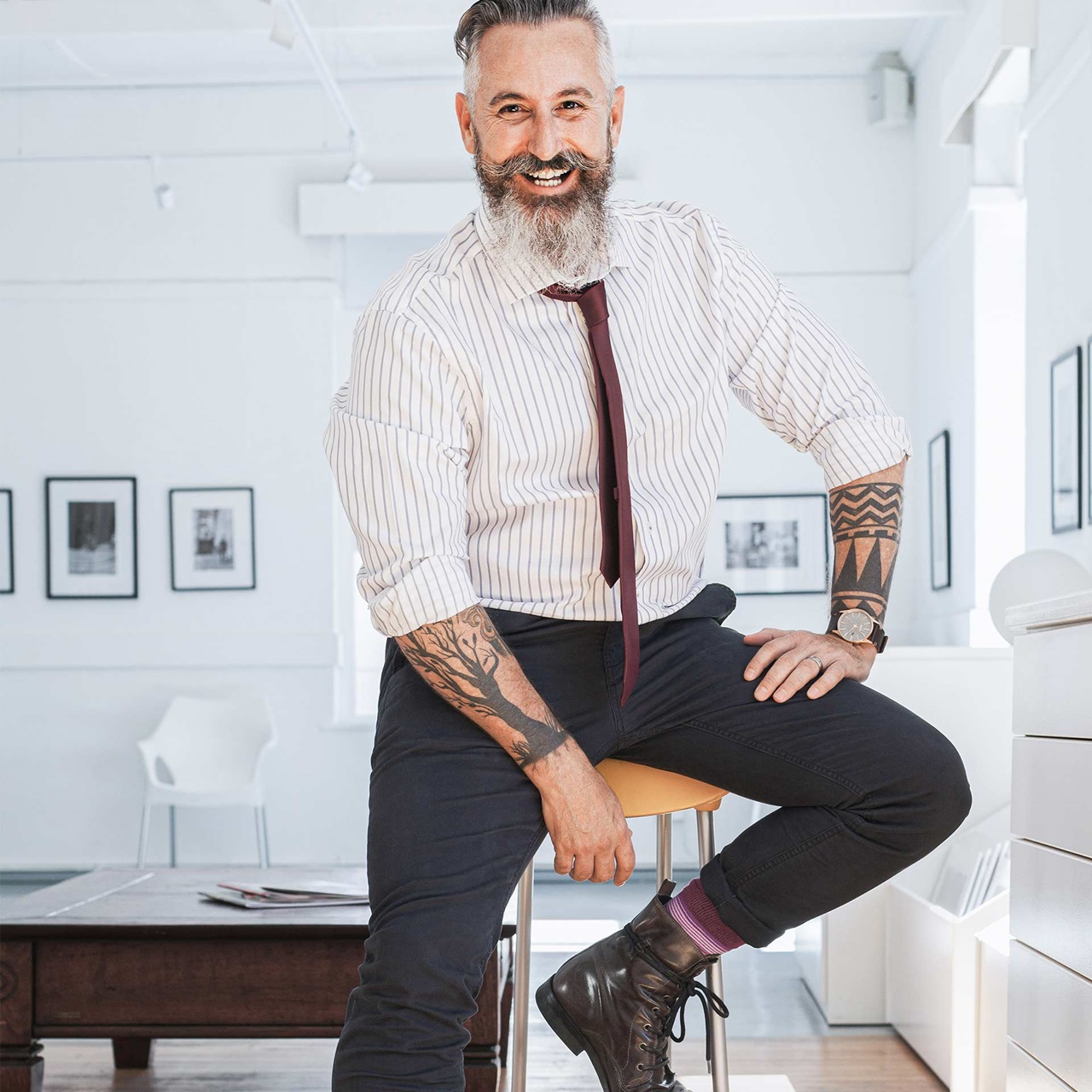 Hipper Businessmann mit Bart und Tattoos sitzt auf einem Hocker und lächelt