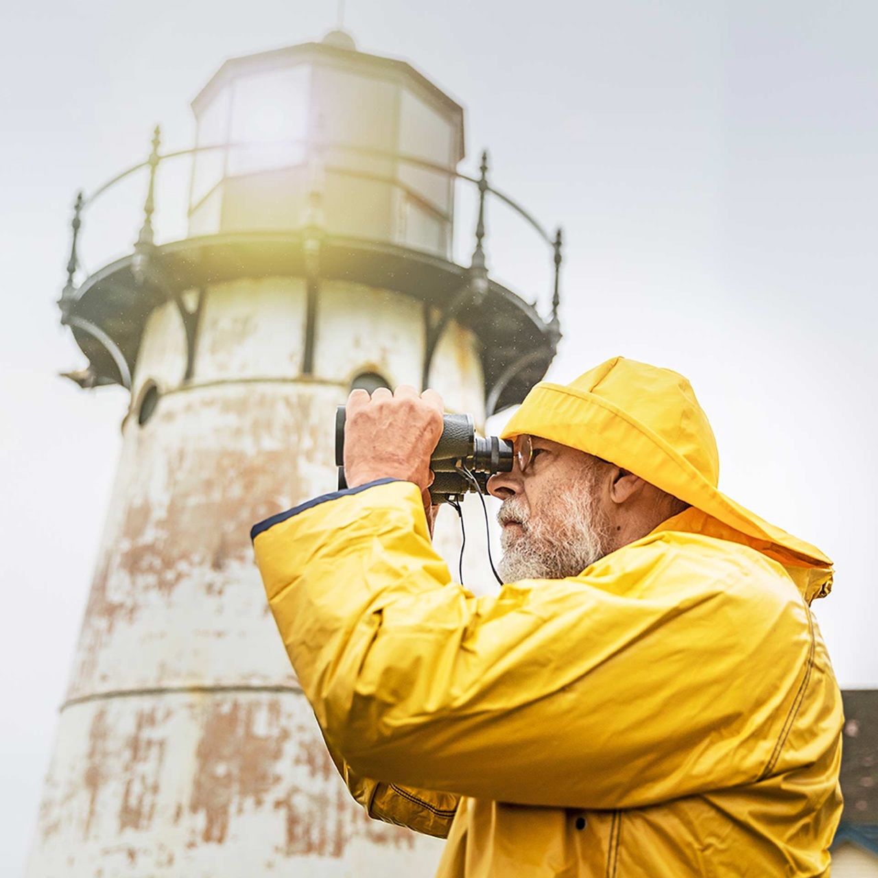 Mann mit Regenjacke und Hut starrt vor einem Leuchtturm durch den Feldstecher