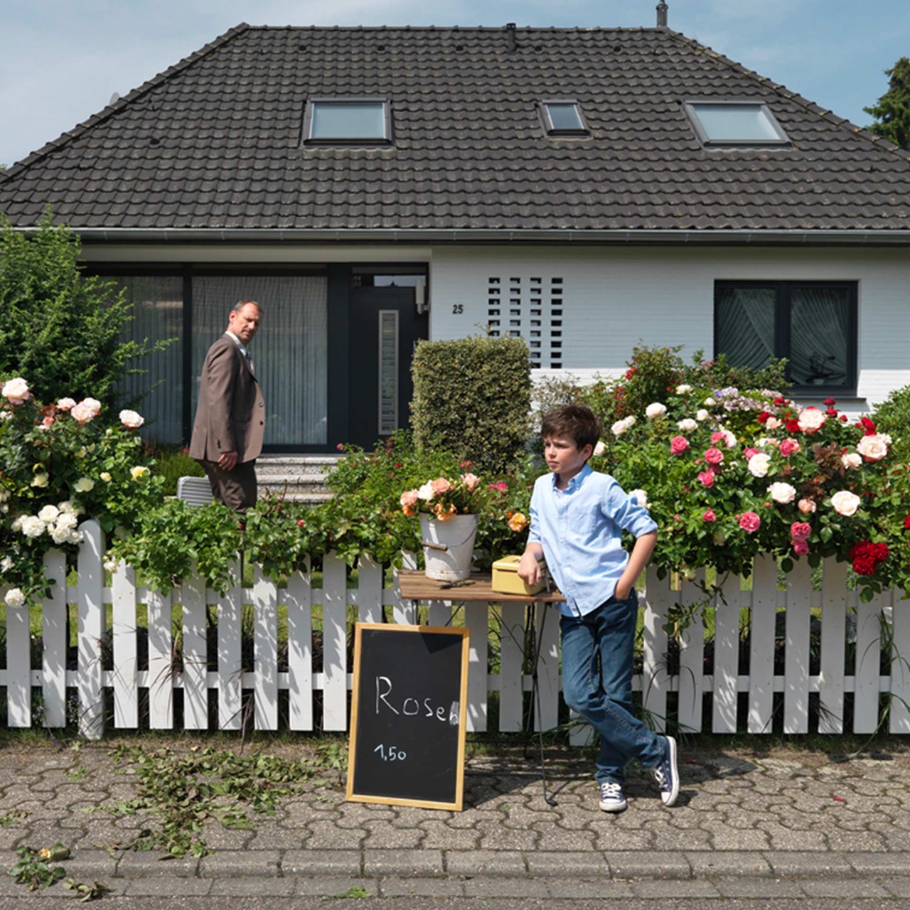 Bub bietet Rosen zum Verkauf vor dem Haus während sein Vater zuschaut
