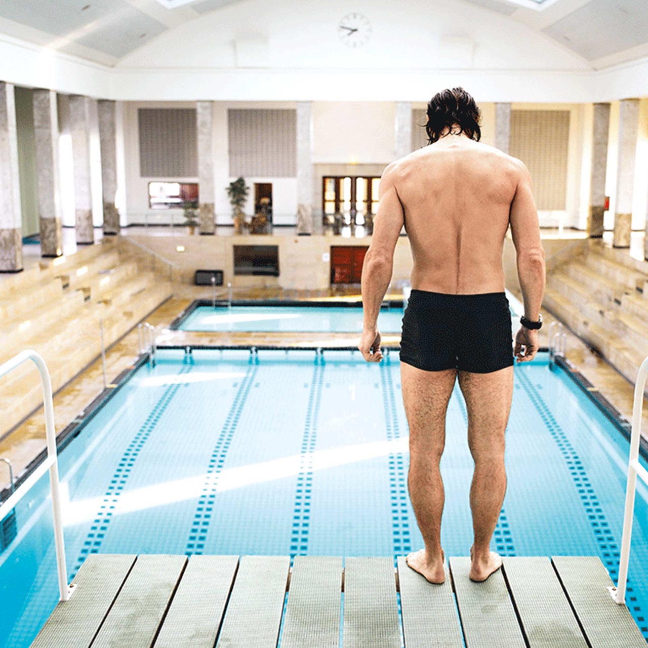 Muskulöser Mann in Badehose steht auf dem Sprungturm im Schwimmband