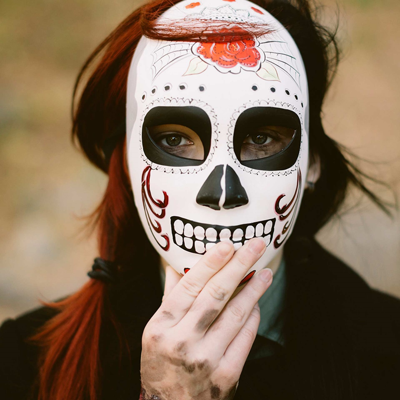 Frau mit langen Haaren hält eine mexikanische Totenmaske vors Gesicht 