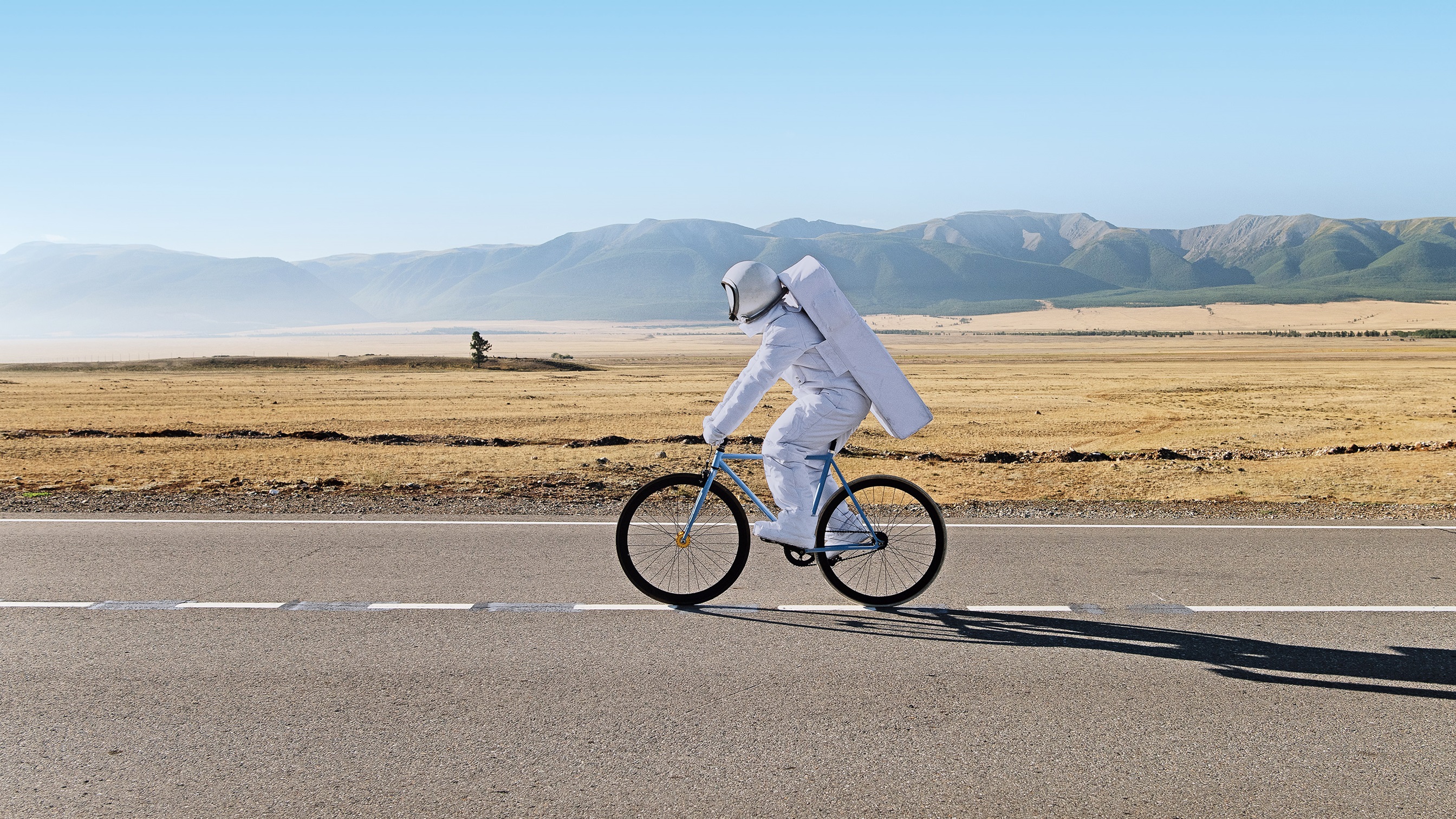 Ein Mann im Astronautanzug, der auf einem Fahrrad in der Wüste fährt