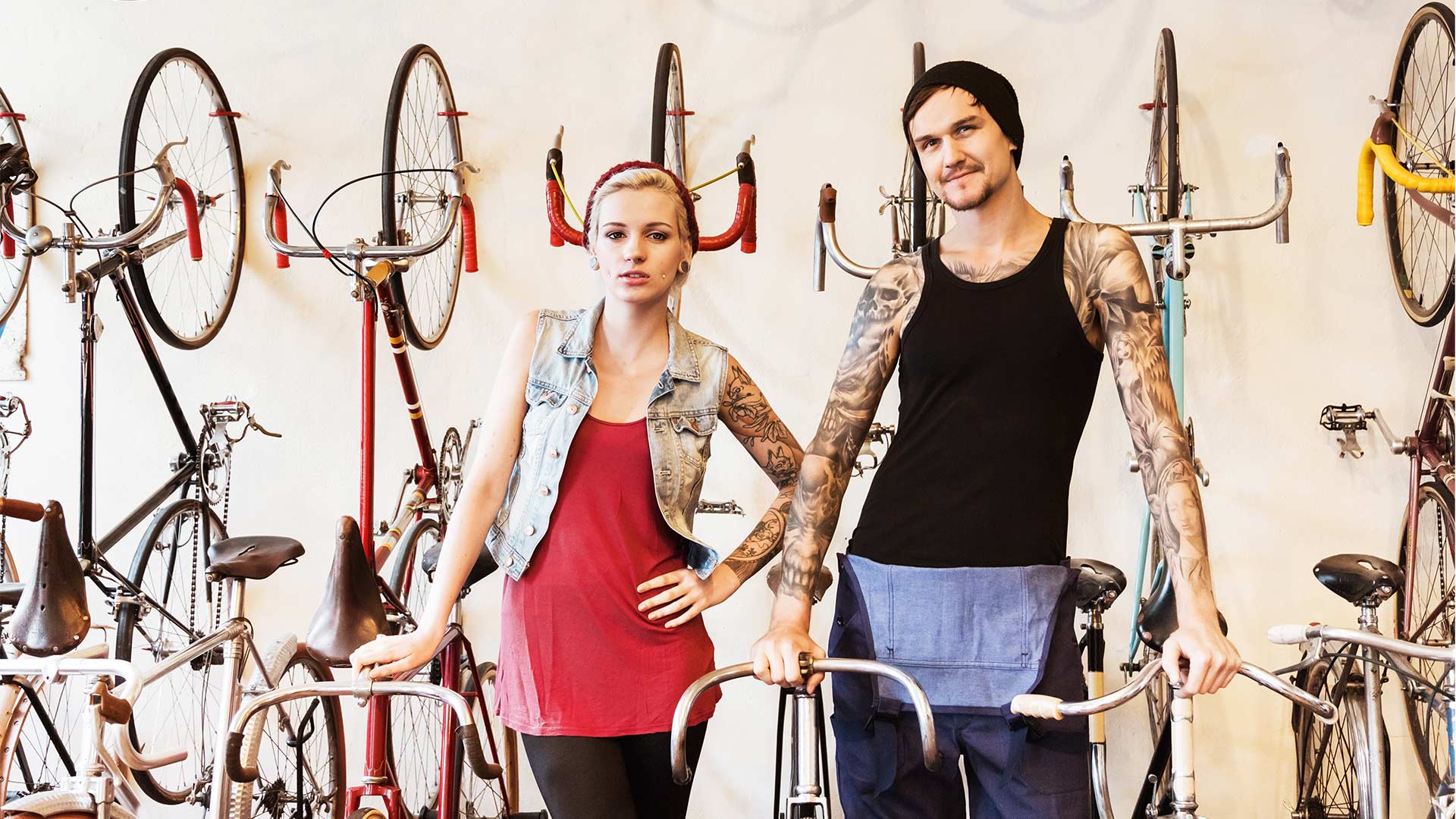 Tätowiertes Paar steht vor aufgehängten Fahrrädern an der Wand