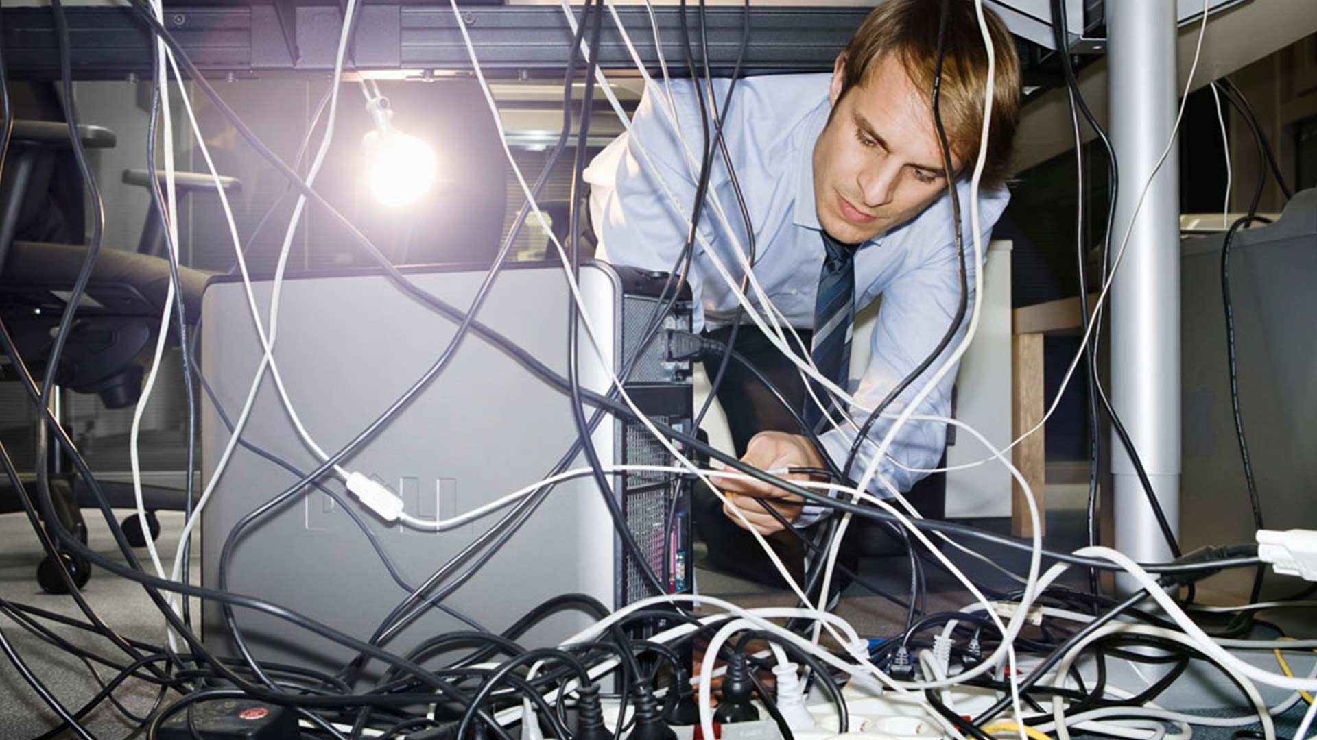Ein junger Mitarbeit versucht den Kabelsalat unter dem Computer zu entwirren