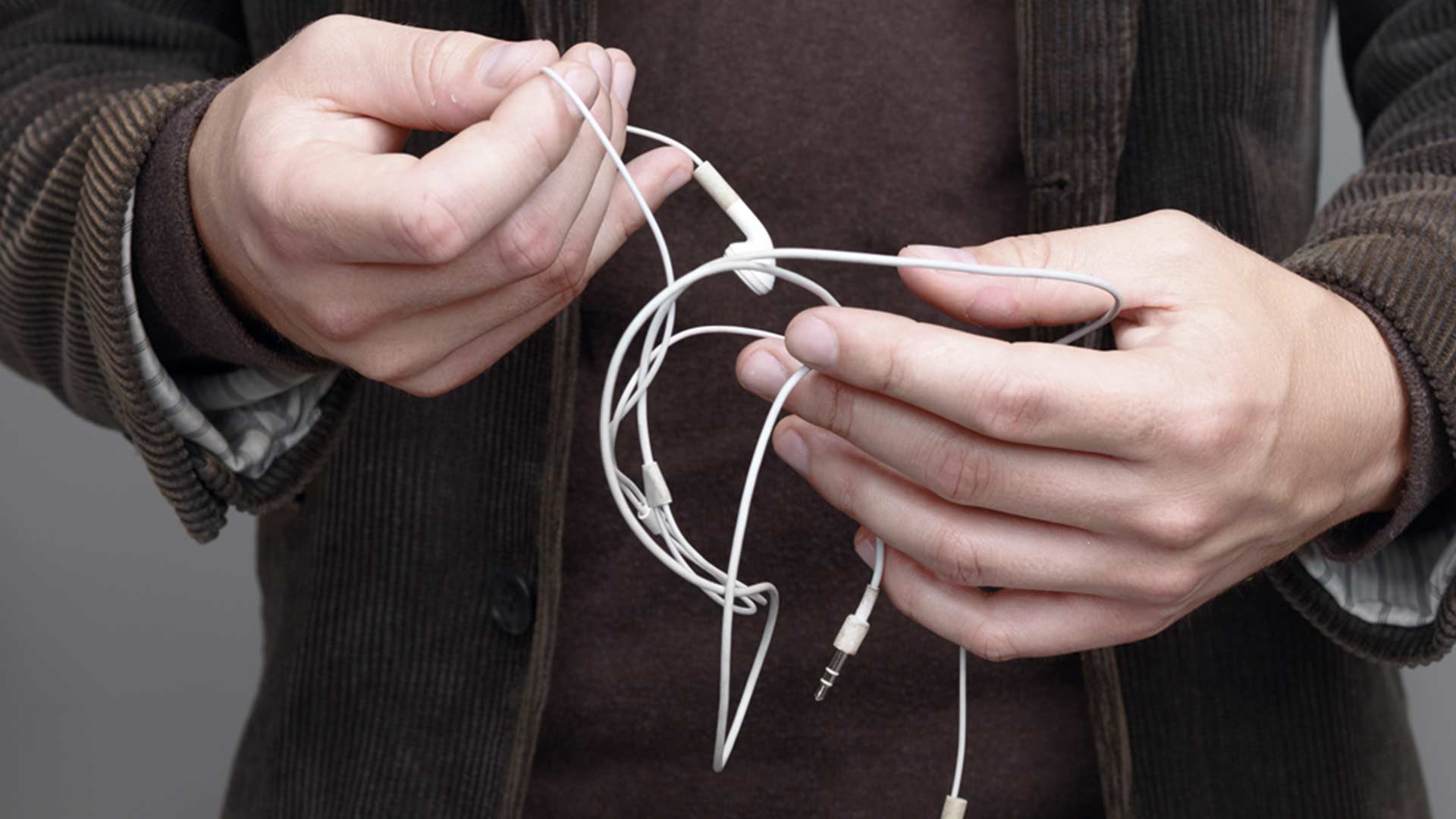 Mann in Kordjacke hält einen iPhone-Kopfhörer mit Kabel in den Händen