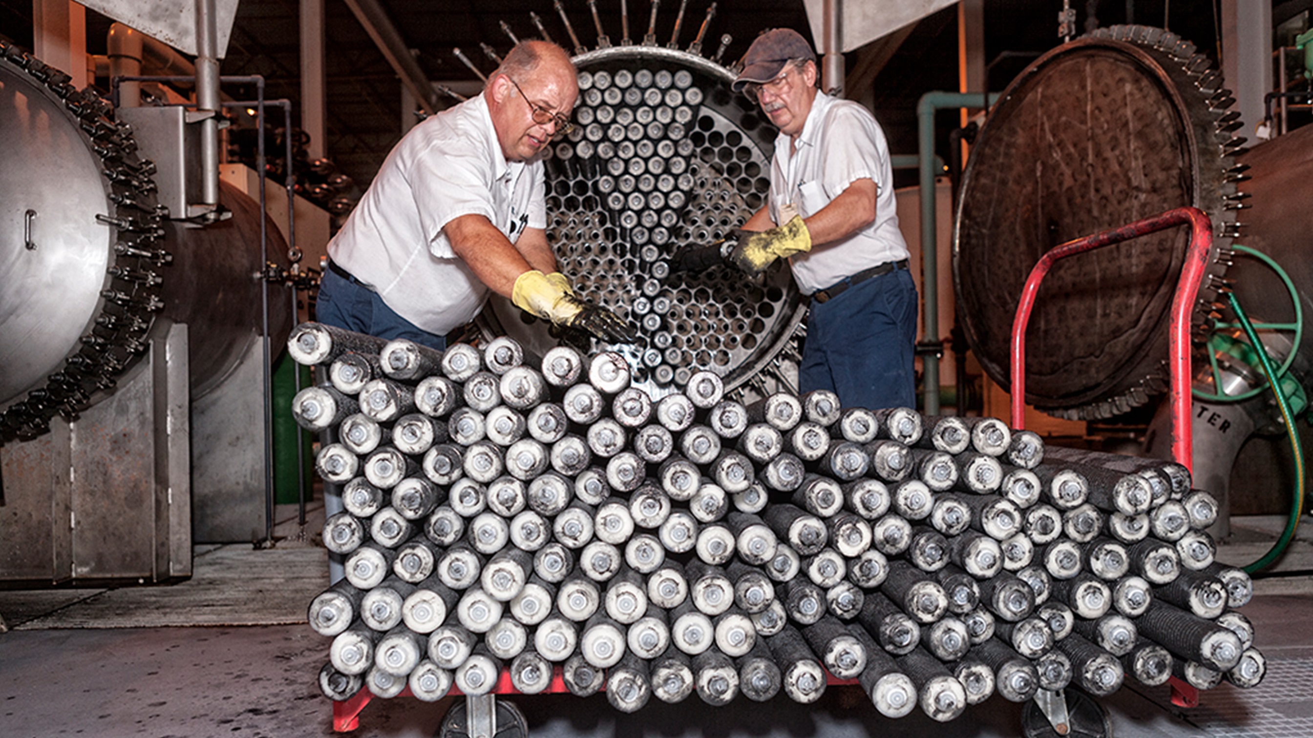 Zwei Männer mit Handschuhen bearbeiten Stahlrohre in einer Fabrik