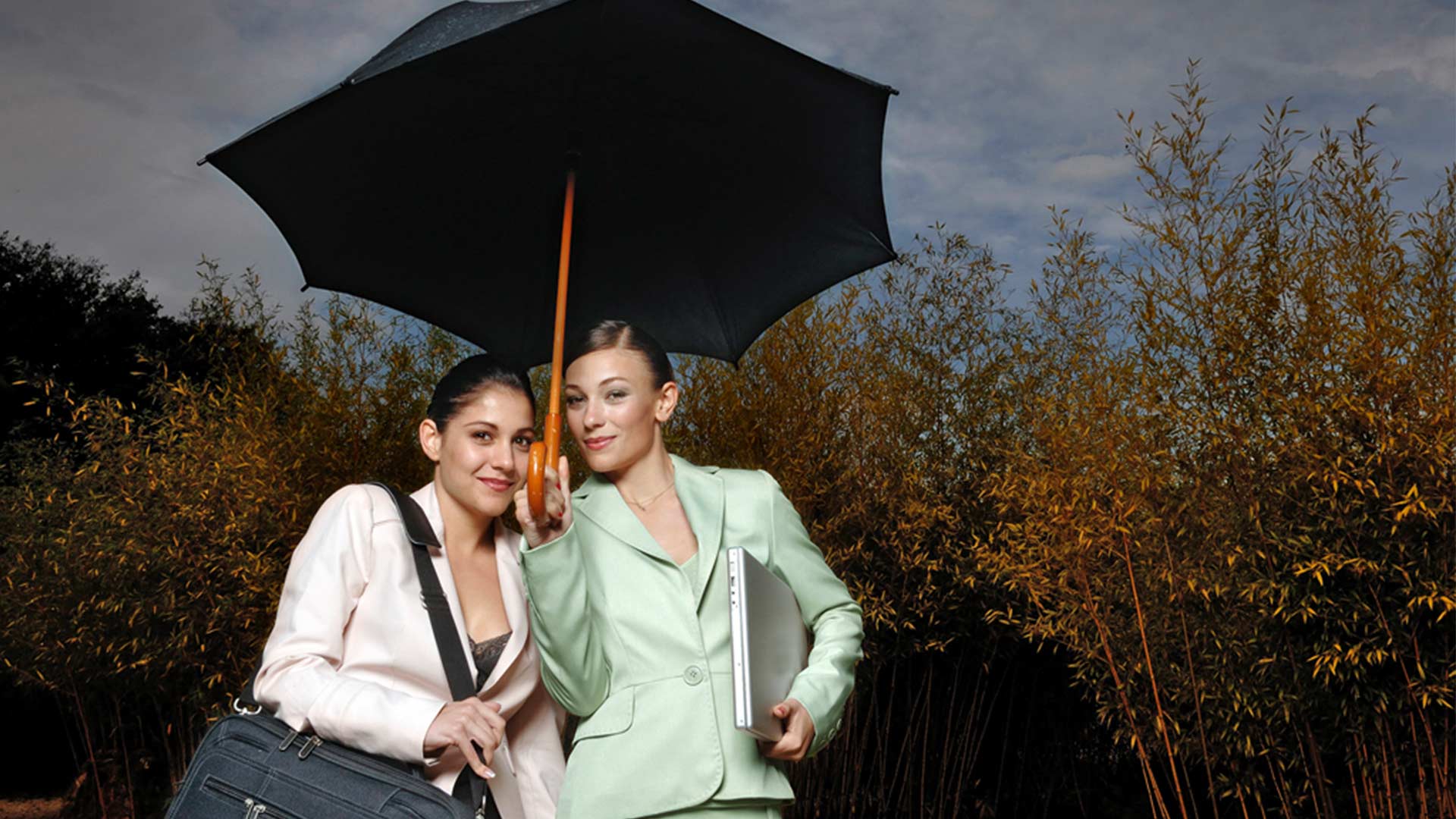 Zwei junge strahlende Geschäftsfrauen stehen unter einem Regenschirm 