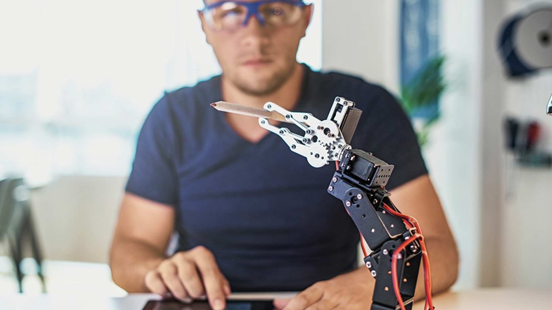 Mann mit Tablet steuert einen Roboter der einen Buntstift hält