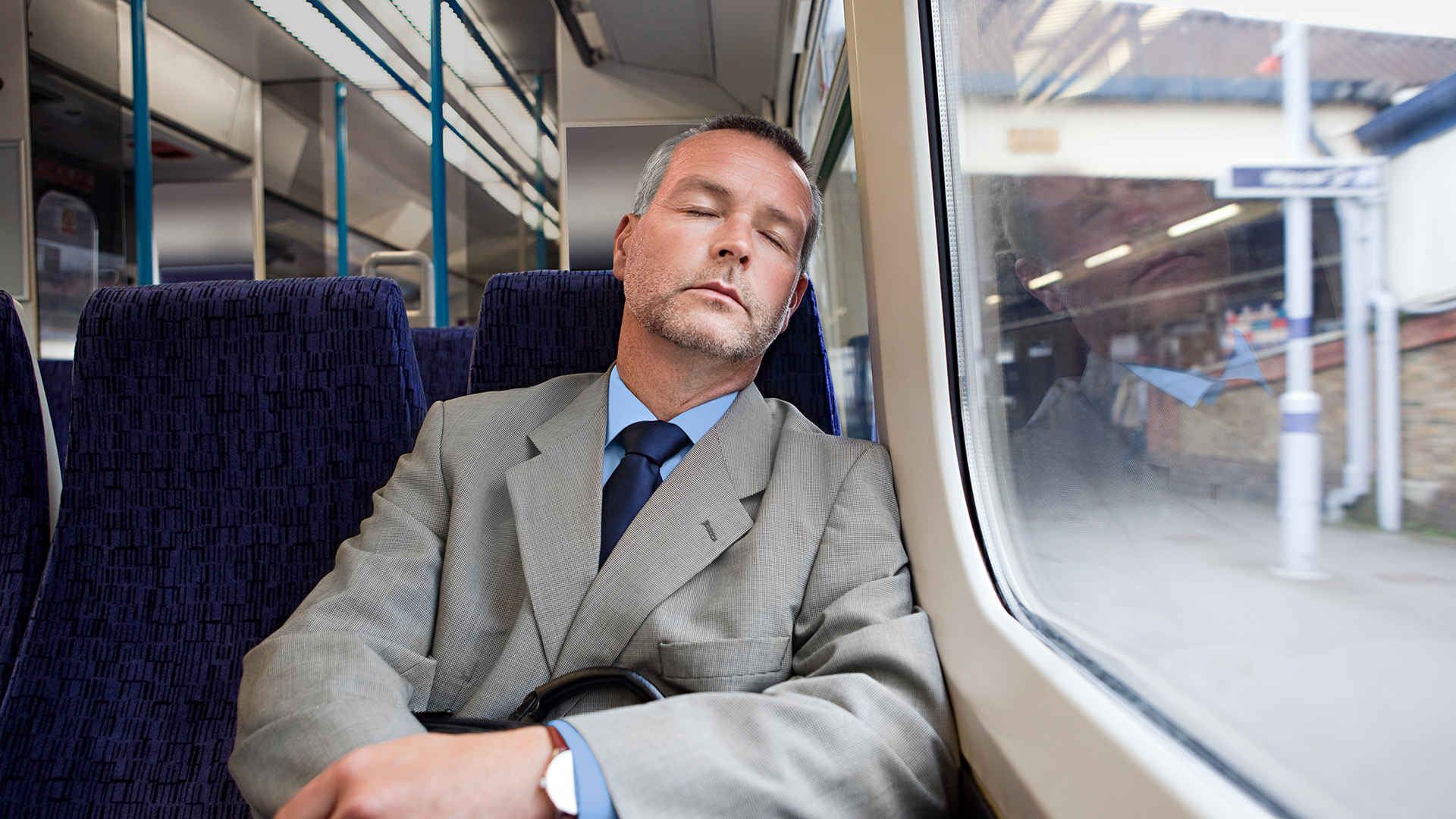 Mann im Anzug sitzend im Zug und am schlafen