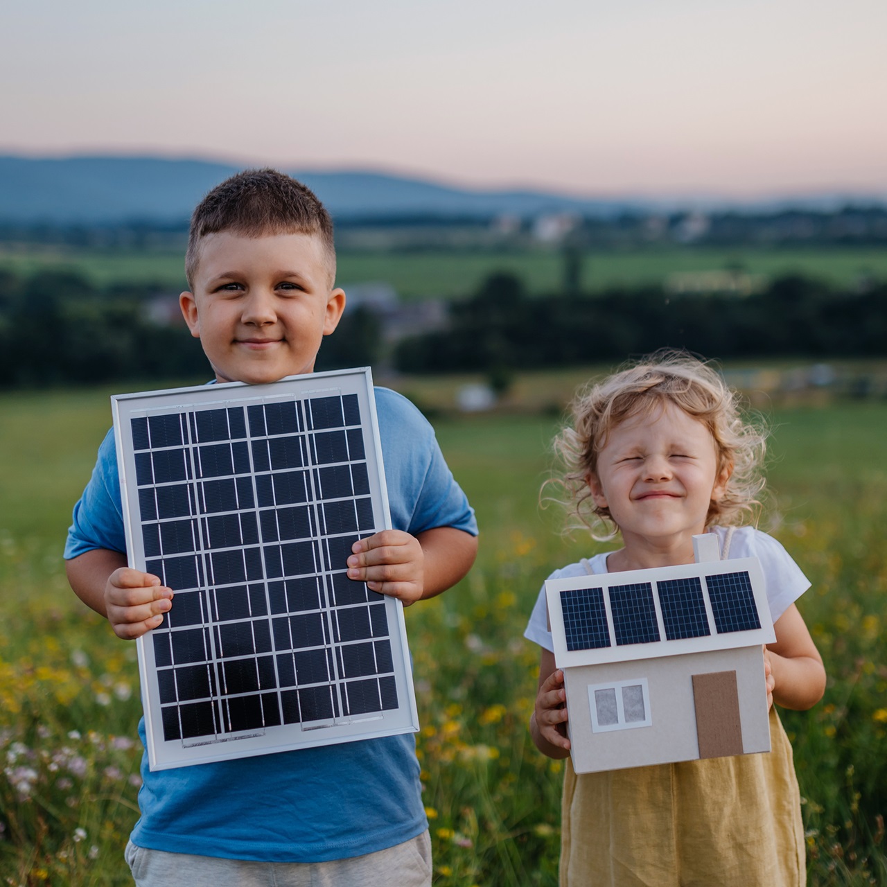 Ein Junge und ein Mädchen stehen auf einem Feld und halten jeweils ein Solarpanel in der Hand und schauen fröhlich in die Kamera.