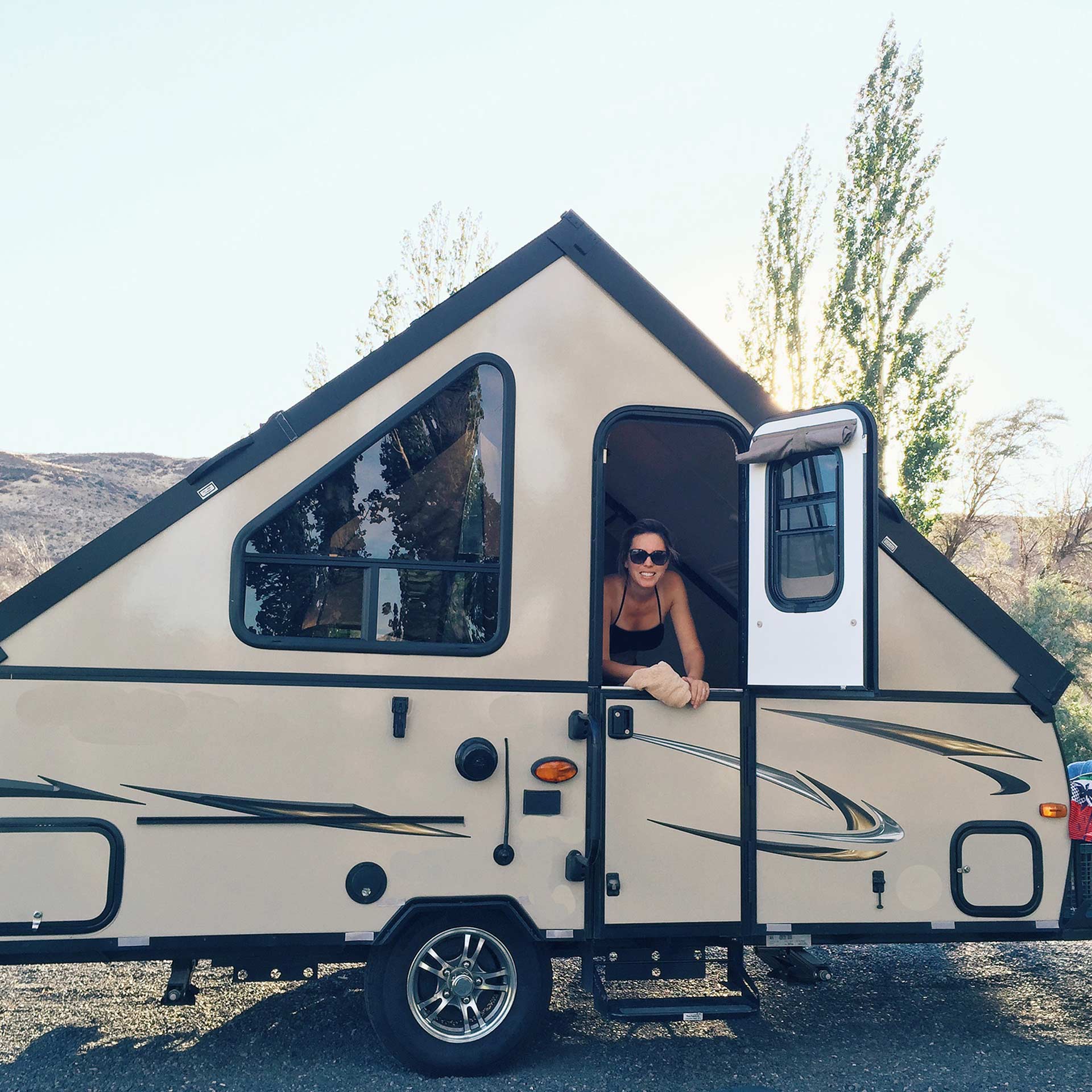 Junge Frau schaut aus einem Autoanhänger in Form eines Dachs fröhlich heraus