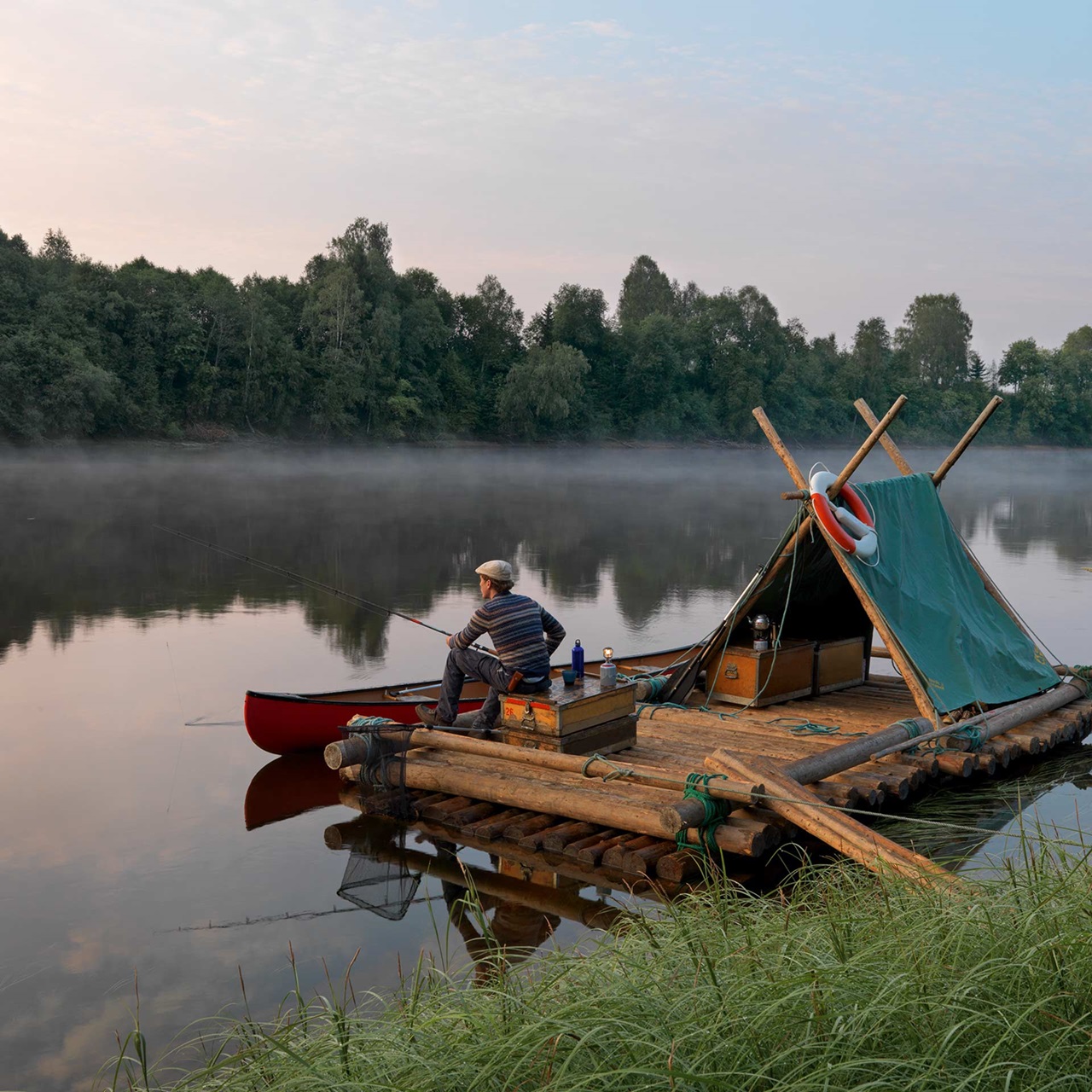 Mann sitzend auf einem Floss mit Zelt darauf, der auf einem See schwimmt