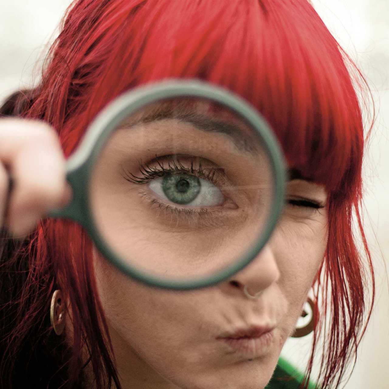 Junge Frau hält sich eine Lupe vors Auge welches riesig erscheint