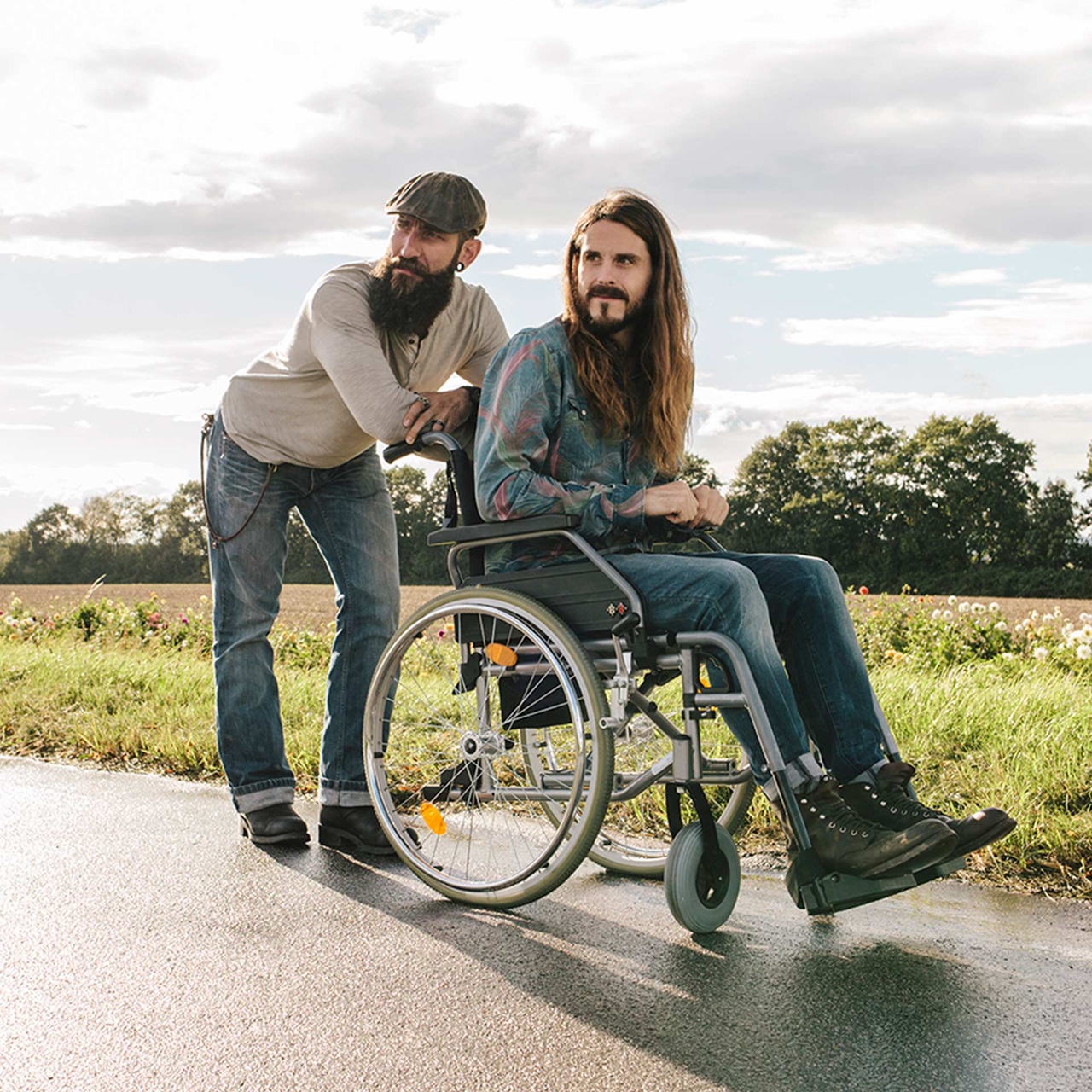 Mann mit Bart und Mütze schiebt einen Mann mit Bart im Rollstuhl