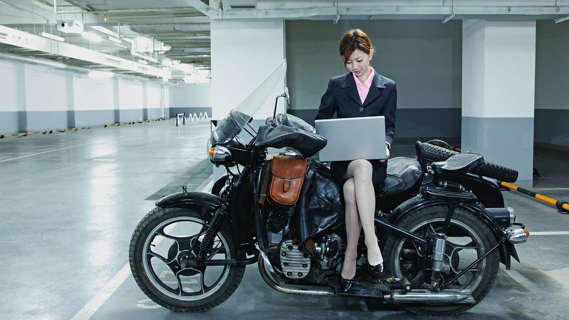 Businessfrau seitlich sitzend auf einem Motorrad mit Laptop auf ihrem Schoss