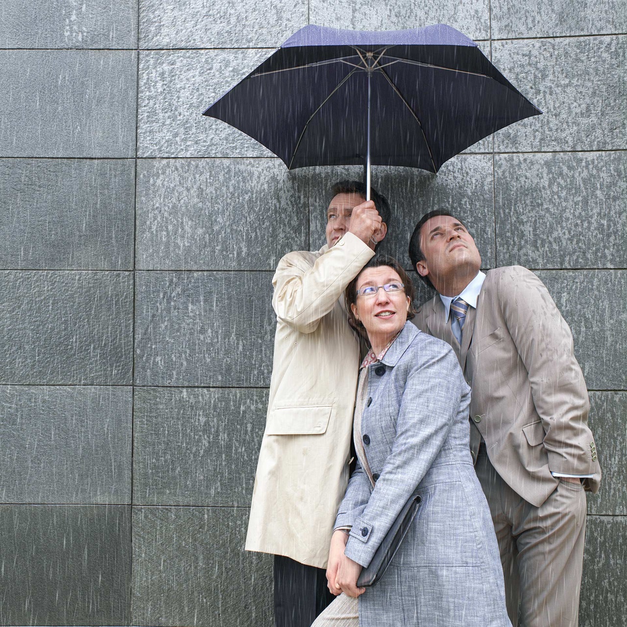 Zwei Männer und eine Frau drängen sich unter einen Regenschirm