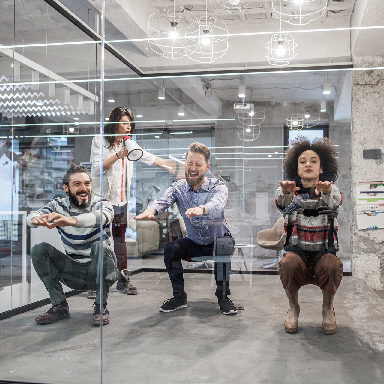 Vier lachende Mitarbeitende machen Fitness in einem Büro