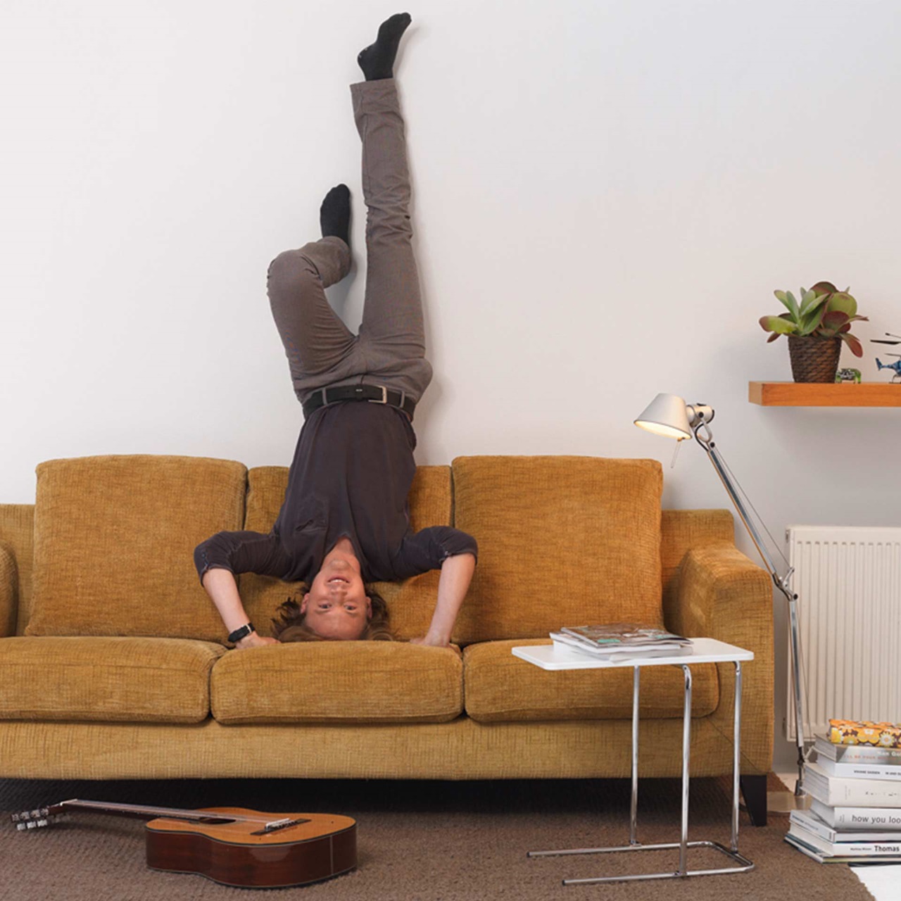 Junger Mann macht einen Handstand auf einem braunen Sofa