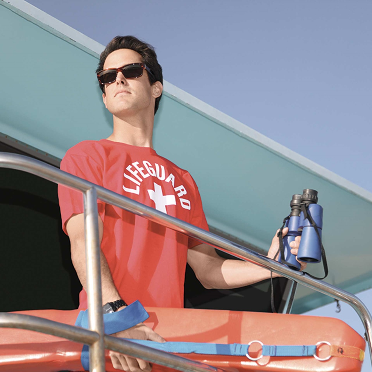 Bademeister im T-Shirt mit Sonnenbrille und Feldstecher passt auf