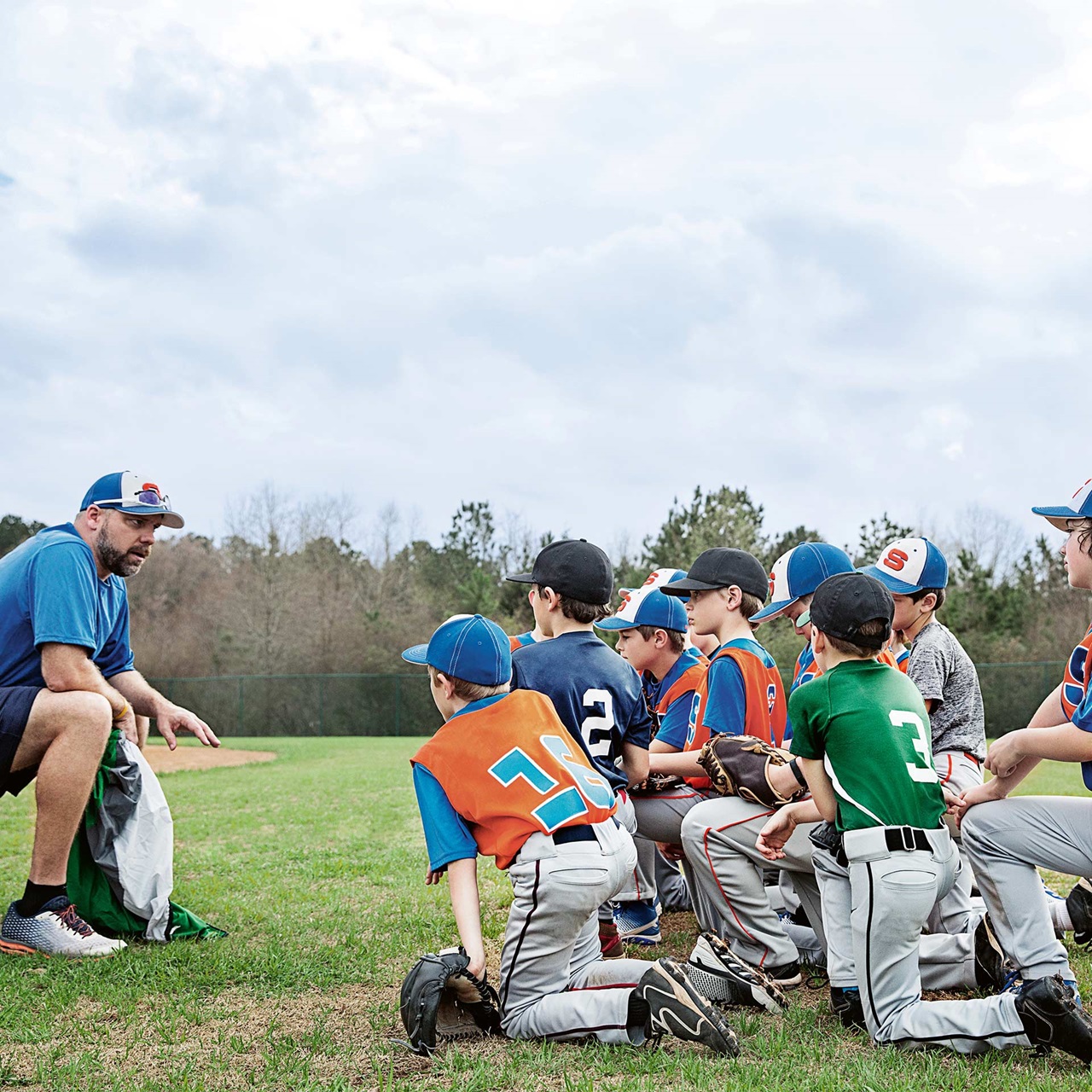 Ein Coach trainiert ein Baseball-Team mit Buben auf einer Wiese