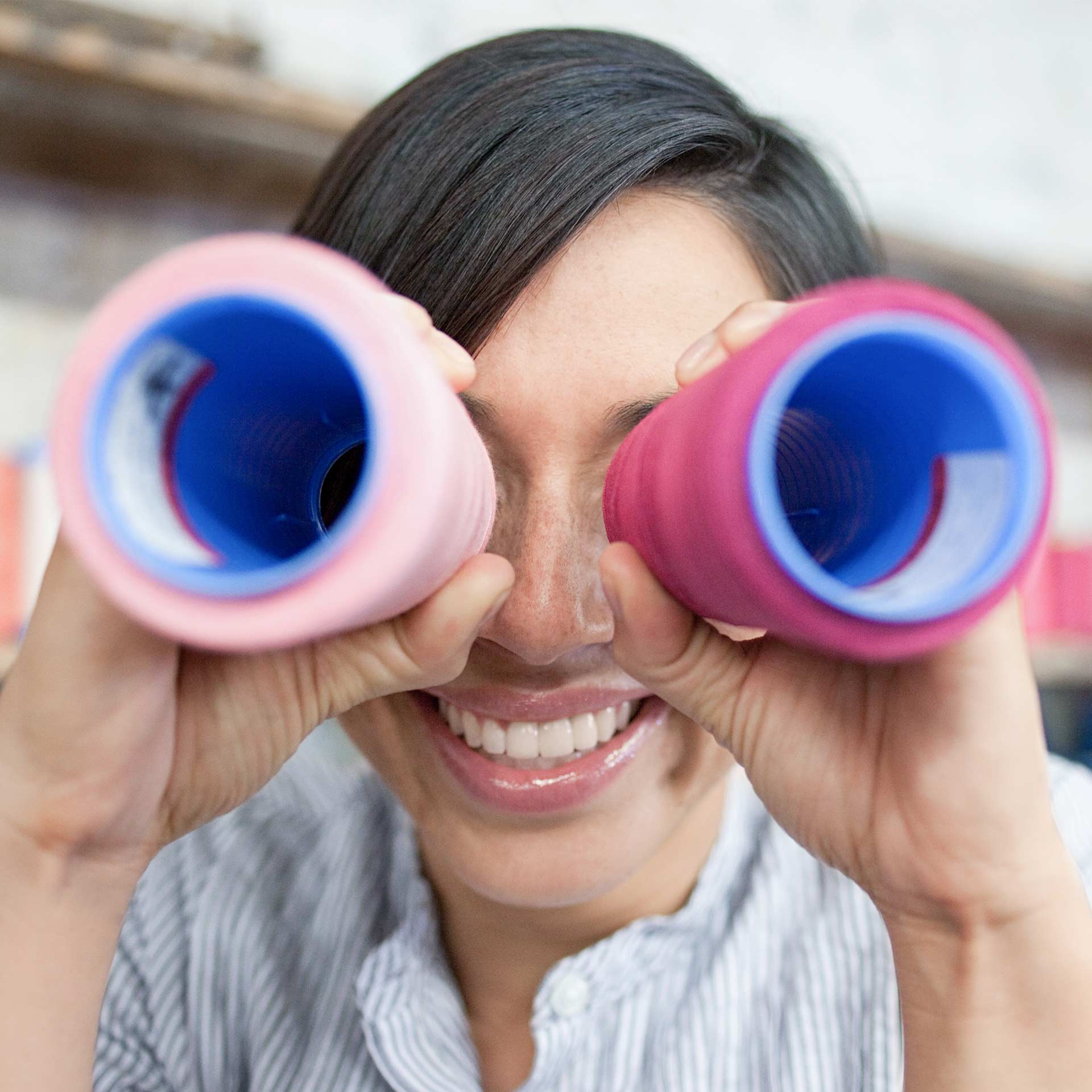 Frau schaut durch zwei bunte Rohre wie durch einen Feldstecher