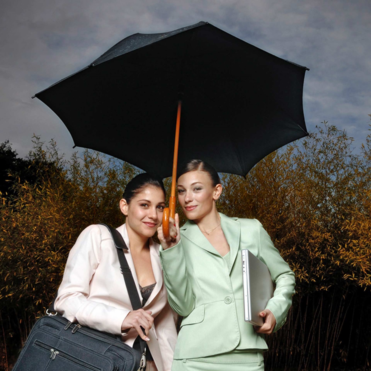 Zwei junge strahlende Geschäftsfrauen stehen unter einem Regenschirm