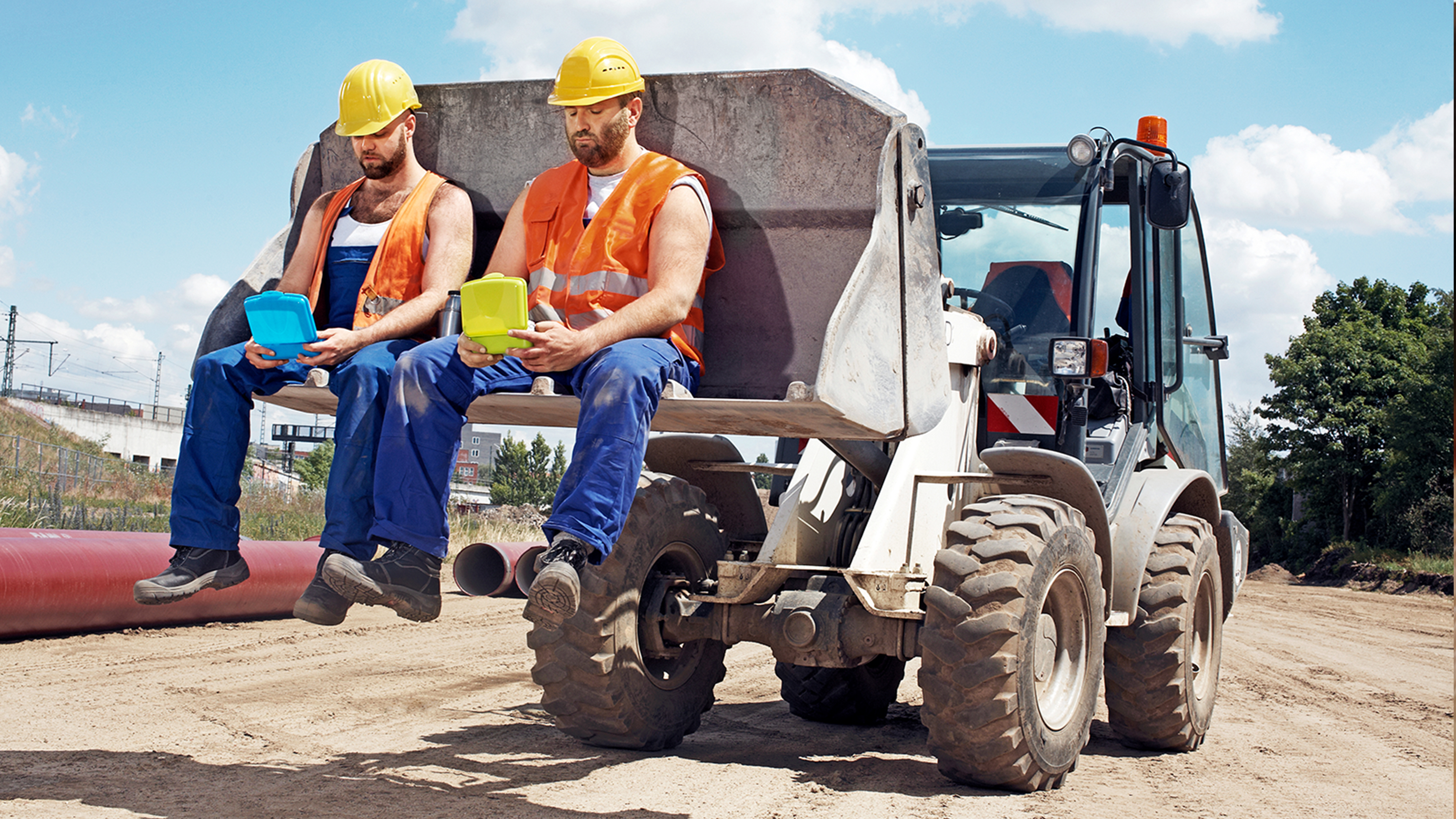 Zwei Bauarbeiter sitzend auf einer Baggerschaufel und starren ihre Lunchboxen an
