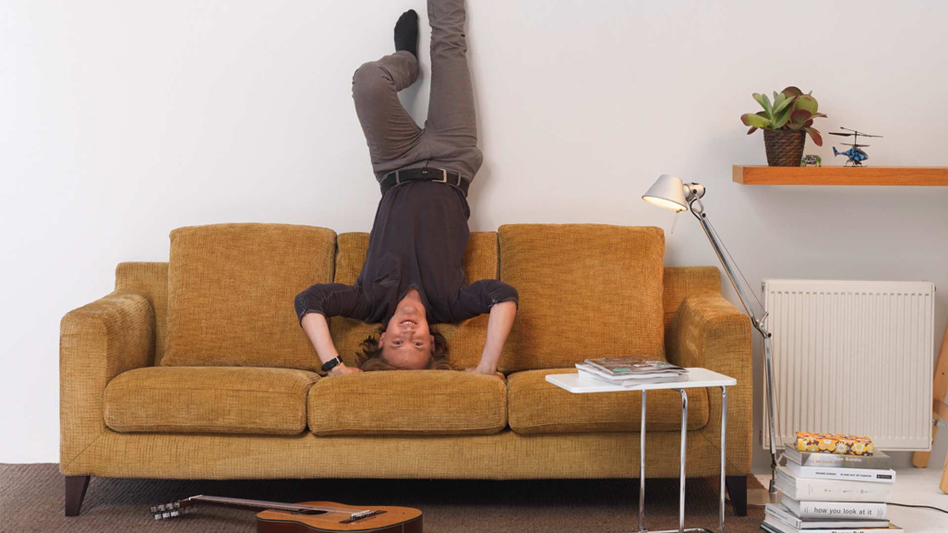 Junger Mann macht einen Handstand auf einem braunen Sofa
