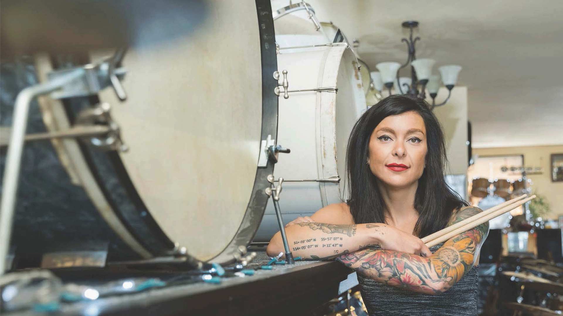 Tätowierte Musikerin mit Trommelstöcken steht im Schlagzeugladen