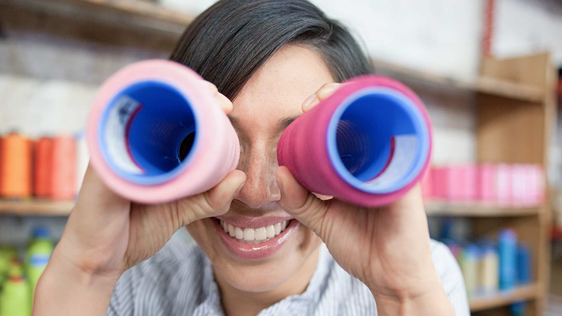 Frau schaut durch zwei bunte Rohre wie durch einen Feldstecher