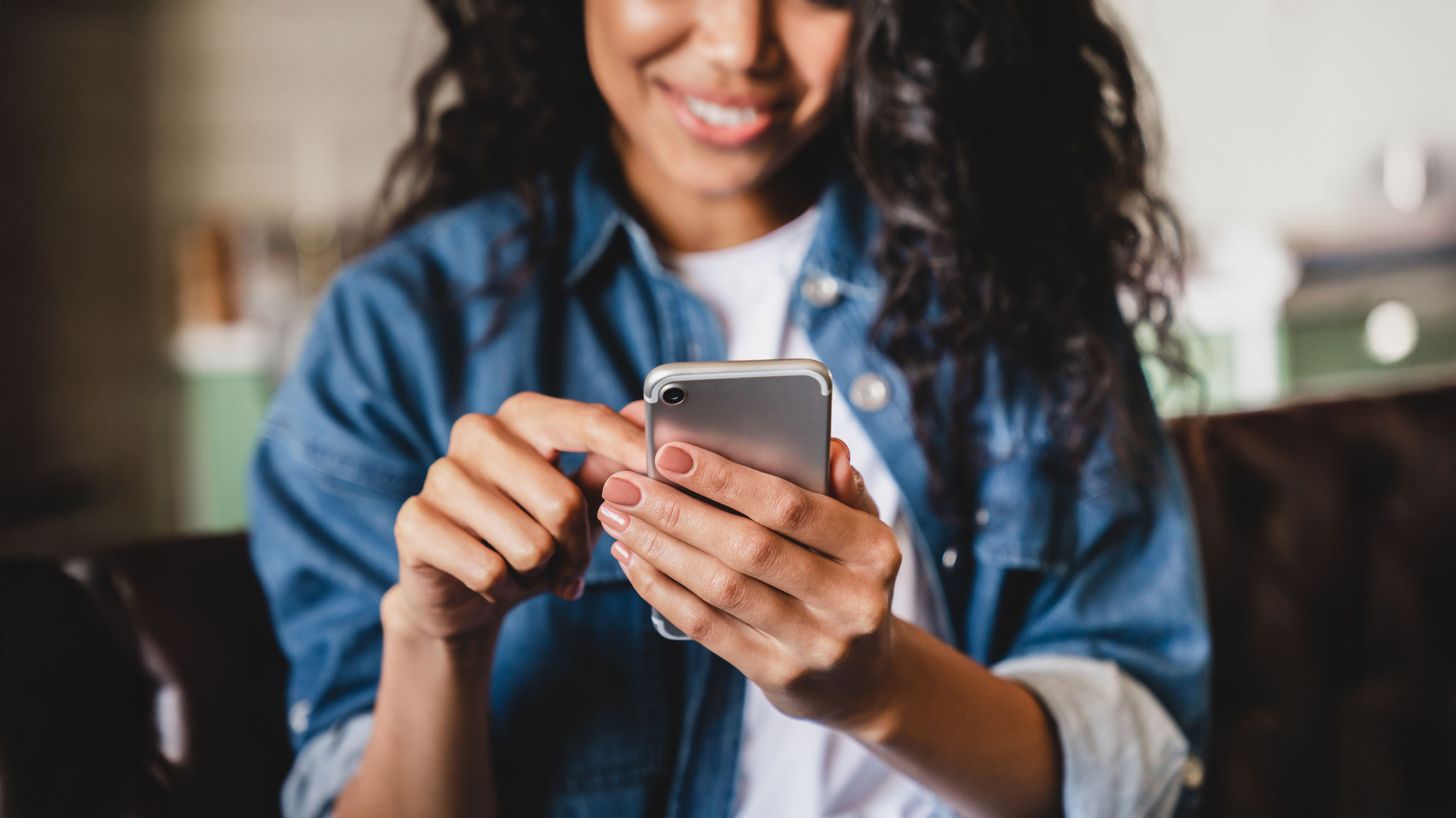 Eine junge lächelnde Frau hält in ihrer Hand ein Smartphone und gibt etwas ein.