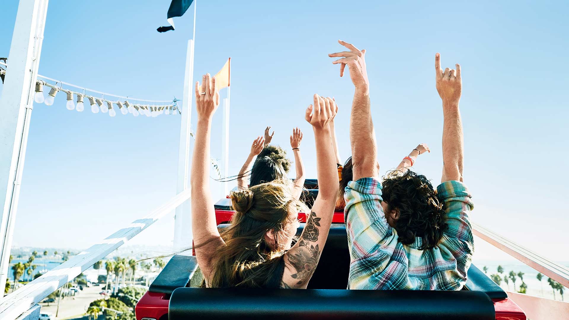 Gruppe von Leuten hält jubelnd die Arme auf einer Achterbahn hoch